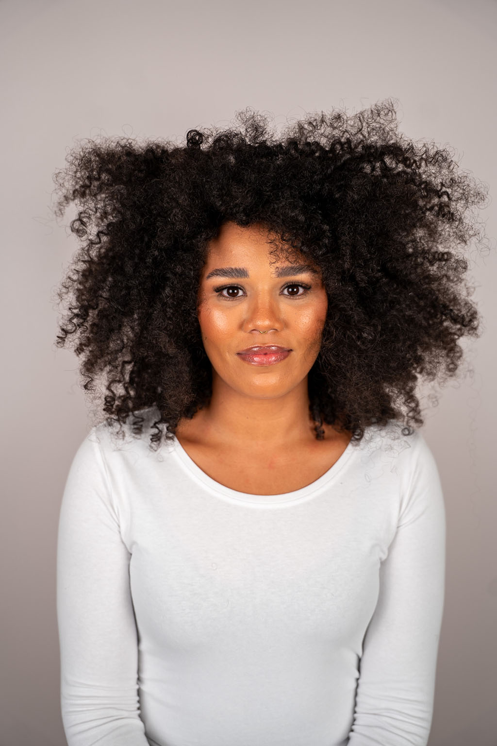 Woman with curly hair wearing a white shirt against a gray background