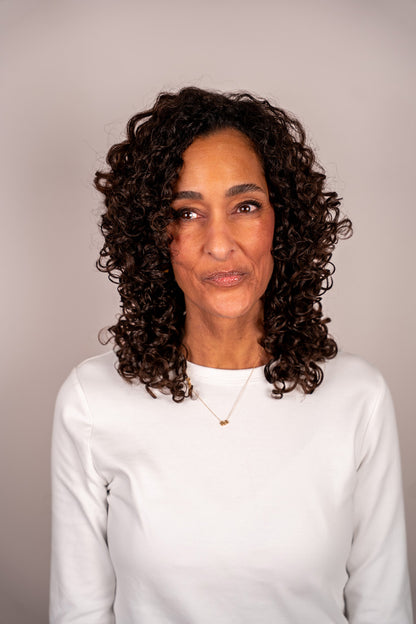 Woman with curly hair wearing a white sweater against a plain background