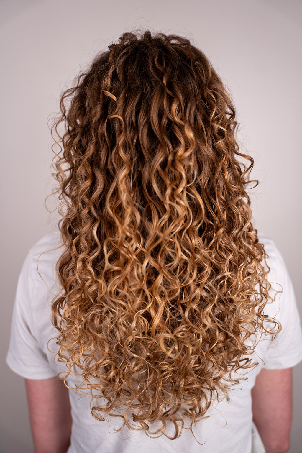 Person with long, wavy, brown hair wearing a white shirt against a plain background