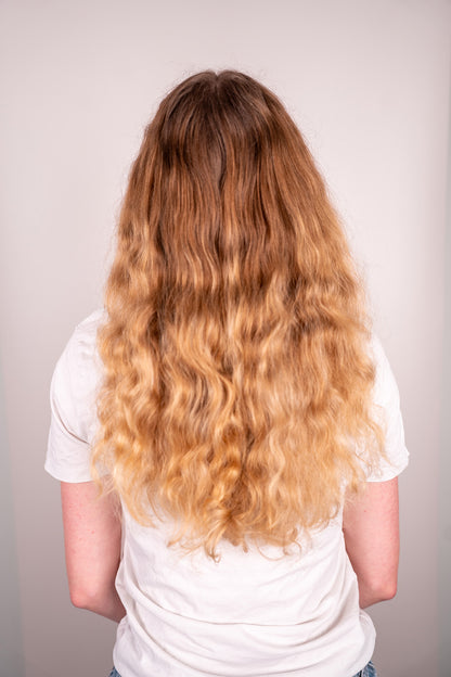 Person with long, wavy blonde hair wearing a white shirt against a plain background