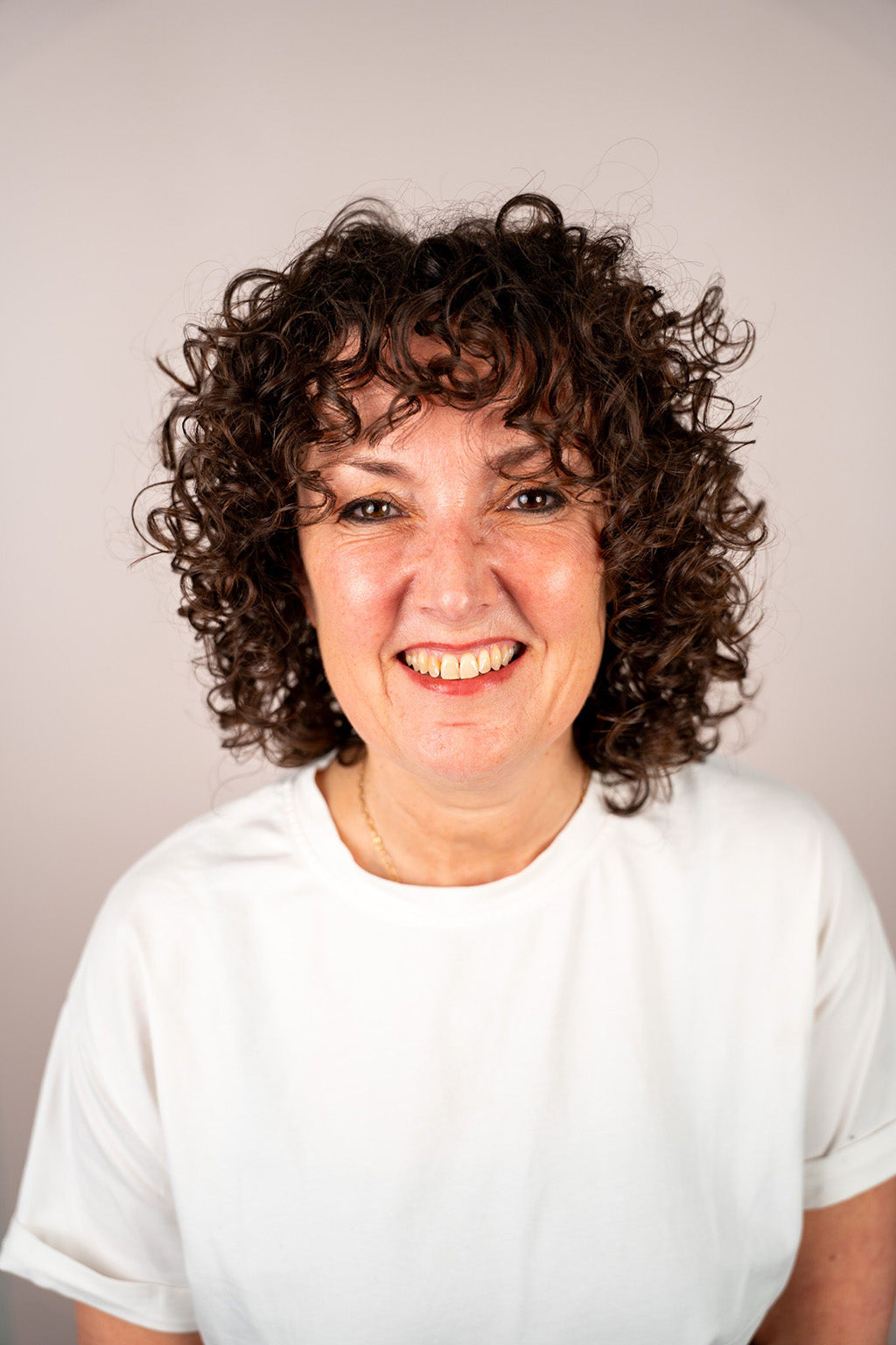 Woman with curly hair wearing a white shirt against a plain background