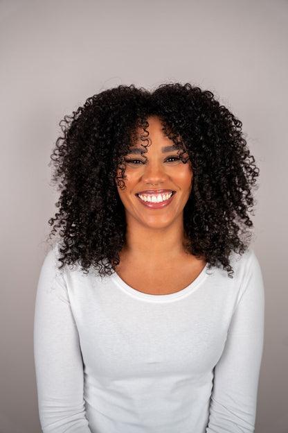Woman with curly hair wearing a light gray long-sleeve shirt against a neutral background