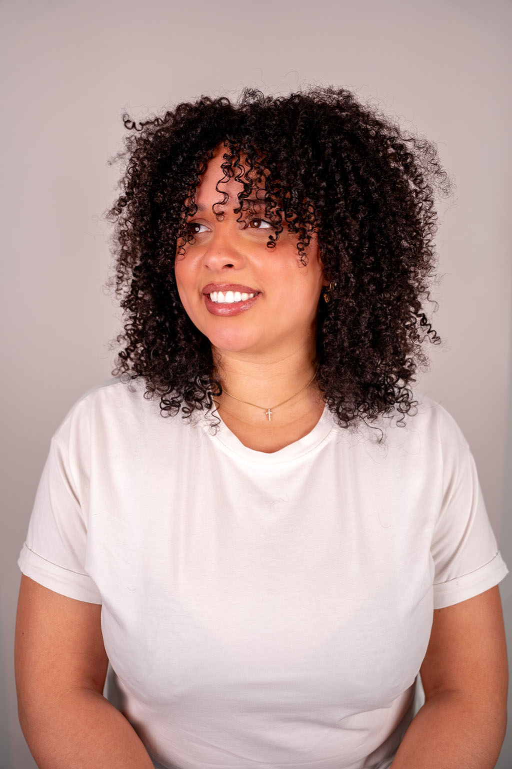Woman with curly hair wearing a white shirt against a plain background