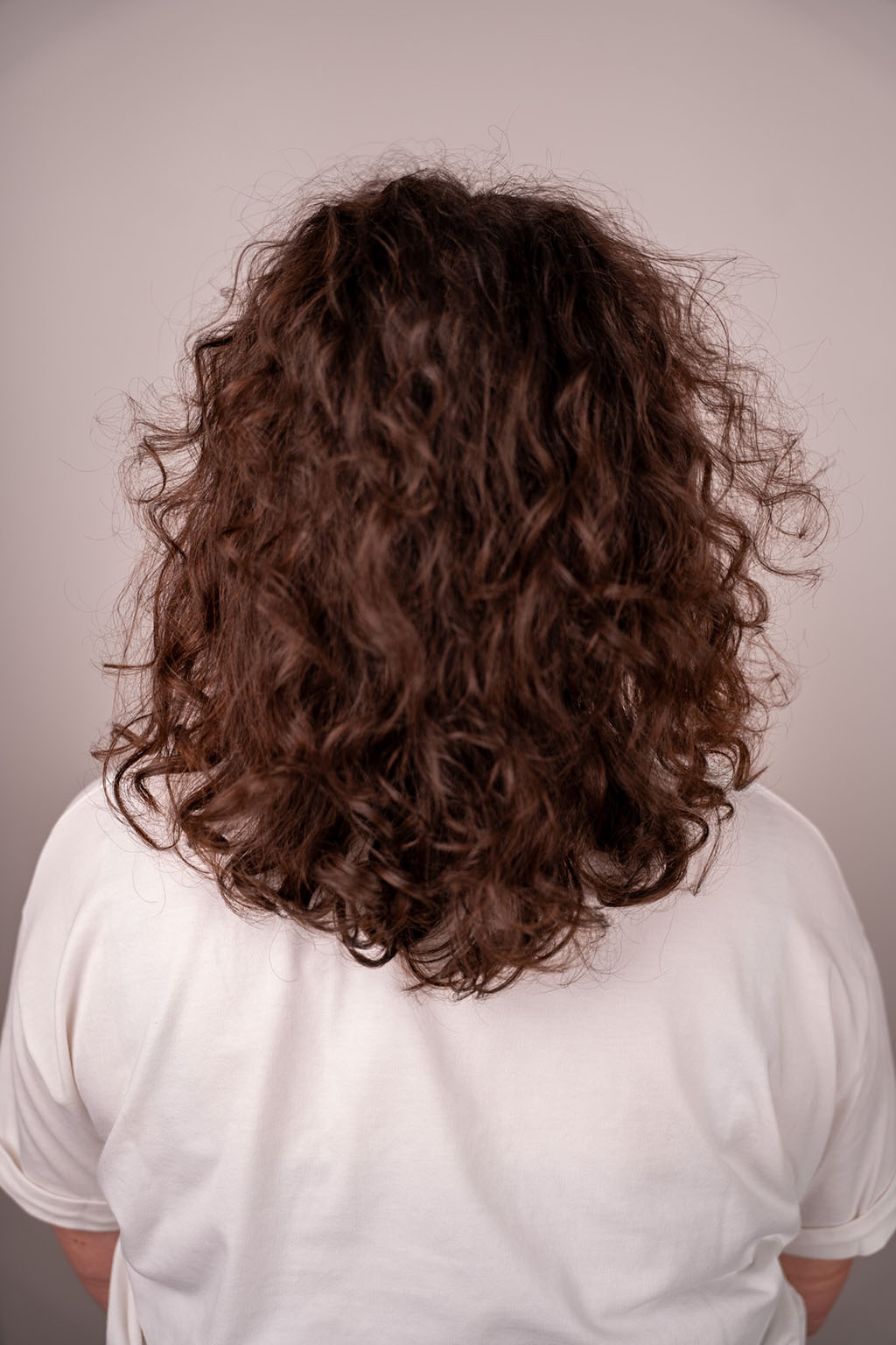 Person with curly brown hair wearing a white shirt against a plain background