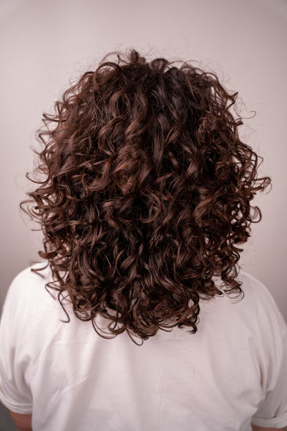 Person with curly brown hair wearing a white shirt against a plain background