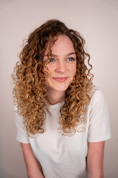Woman with curly hair wearing a white t-shirt against a plain background