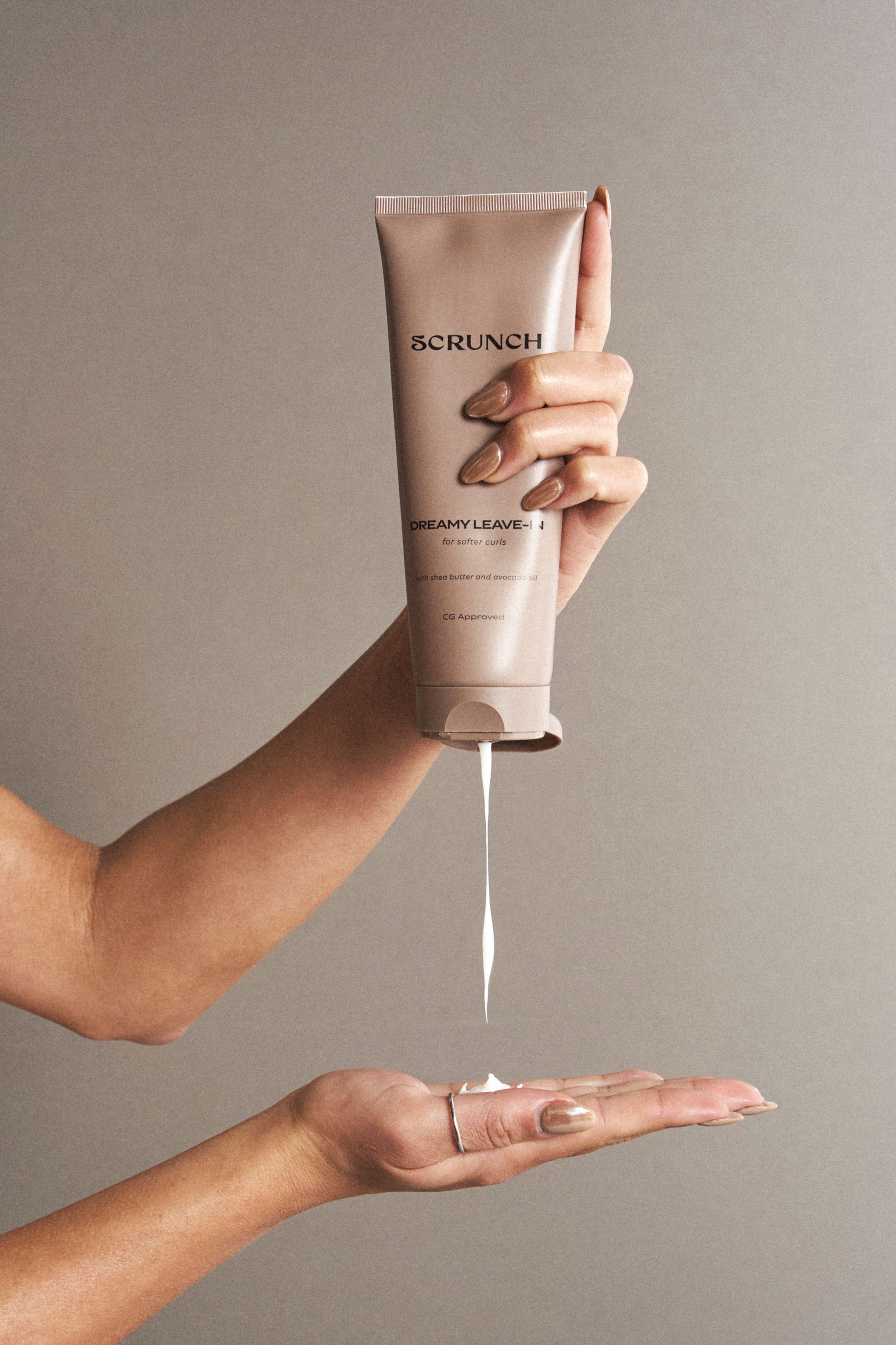 Hand holding a tube of Scrunch hair mask with product dripping onto another hand against a neutral background